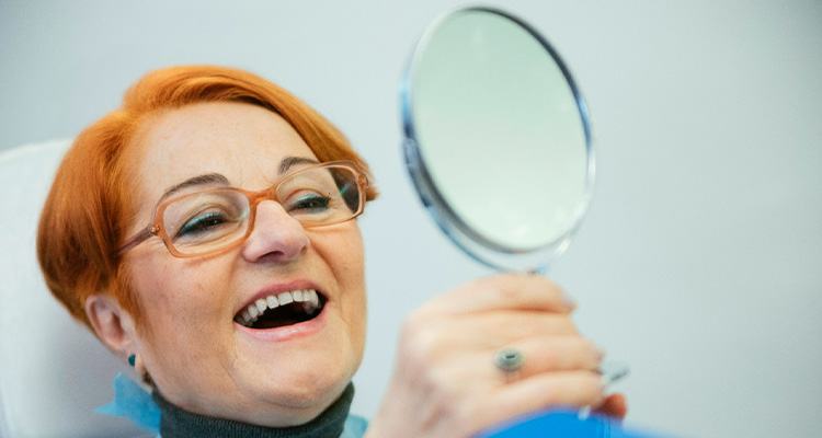 A woman looking at her dentures in the mirror