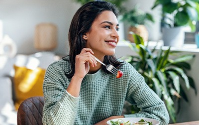Woman in green sweater eating salad at home