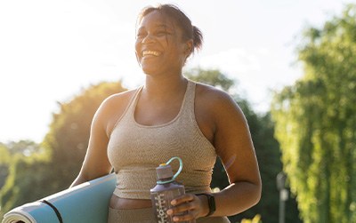 Smiling woman walking with yoga mat and water bottle