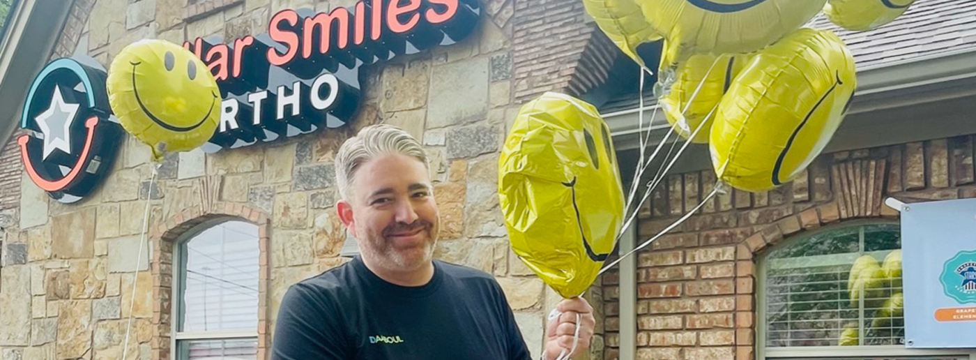 Grapevine cosmetic dentist holding smiley face balloons in front of dental office