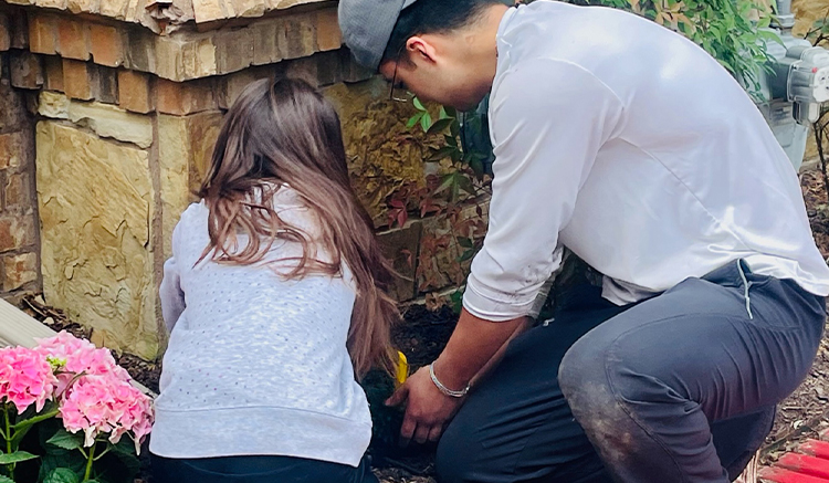 Man helping young girl plant flowers in front of dental office