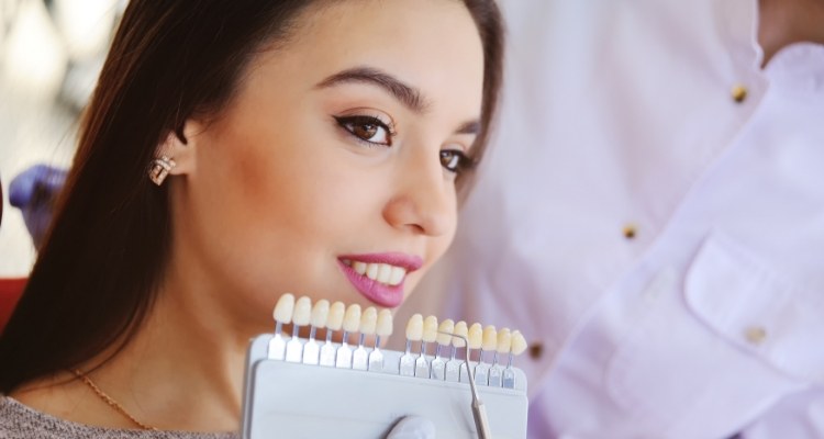 Young woman in dental chair with shade guide for veneers next to her smile