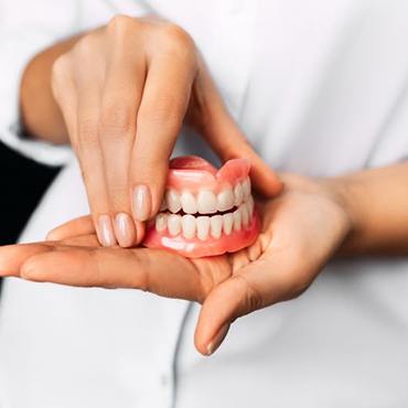 Manicured hands holding full set of dentures