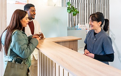 Couple smiling while talking to dental assistant in lobby