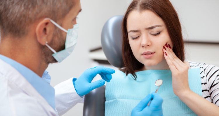 Young woman in dental chair holding her cheek in pain