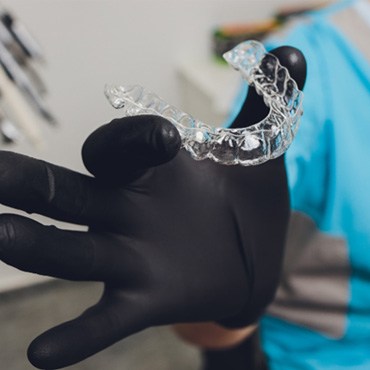 Dentist holding Invisalign aligner with black glove