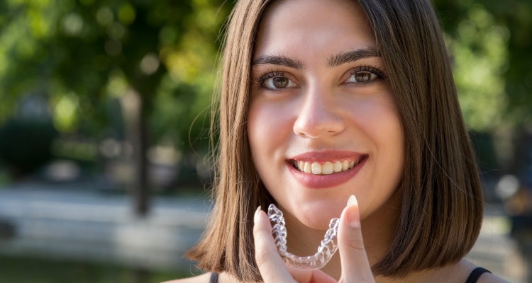 Smiling young woman holding Invisalign tray outdoors