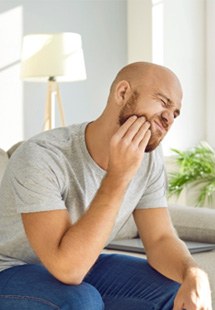 man sitting on couch with jaw pain 