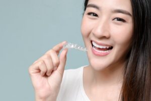 Woman smiling and holding clear aligner. 