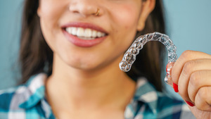 Woman holding clear aligner for Invisalign refinements