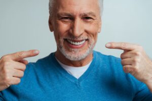 Senior man smiling and pointing to dentures. 